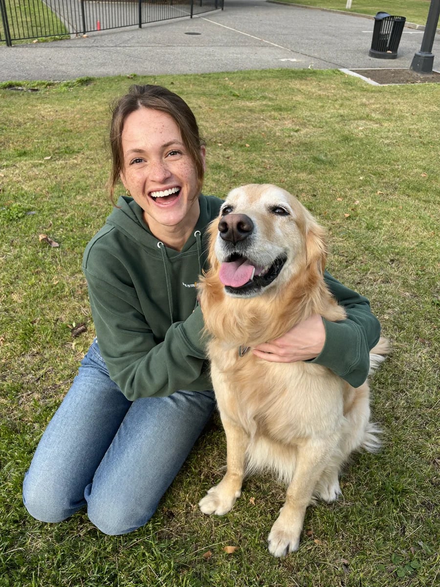 Sophie laughing on the grass in a park with her golden retriever