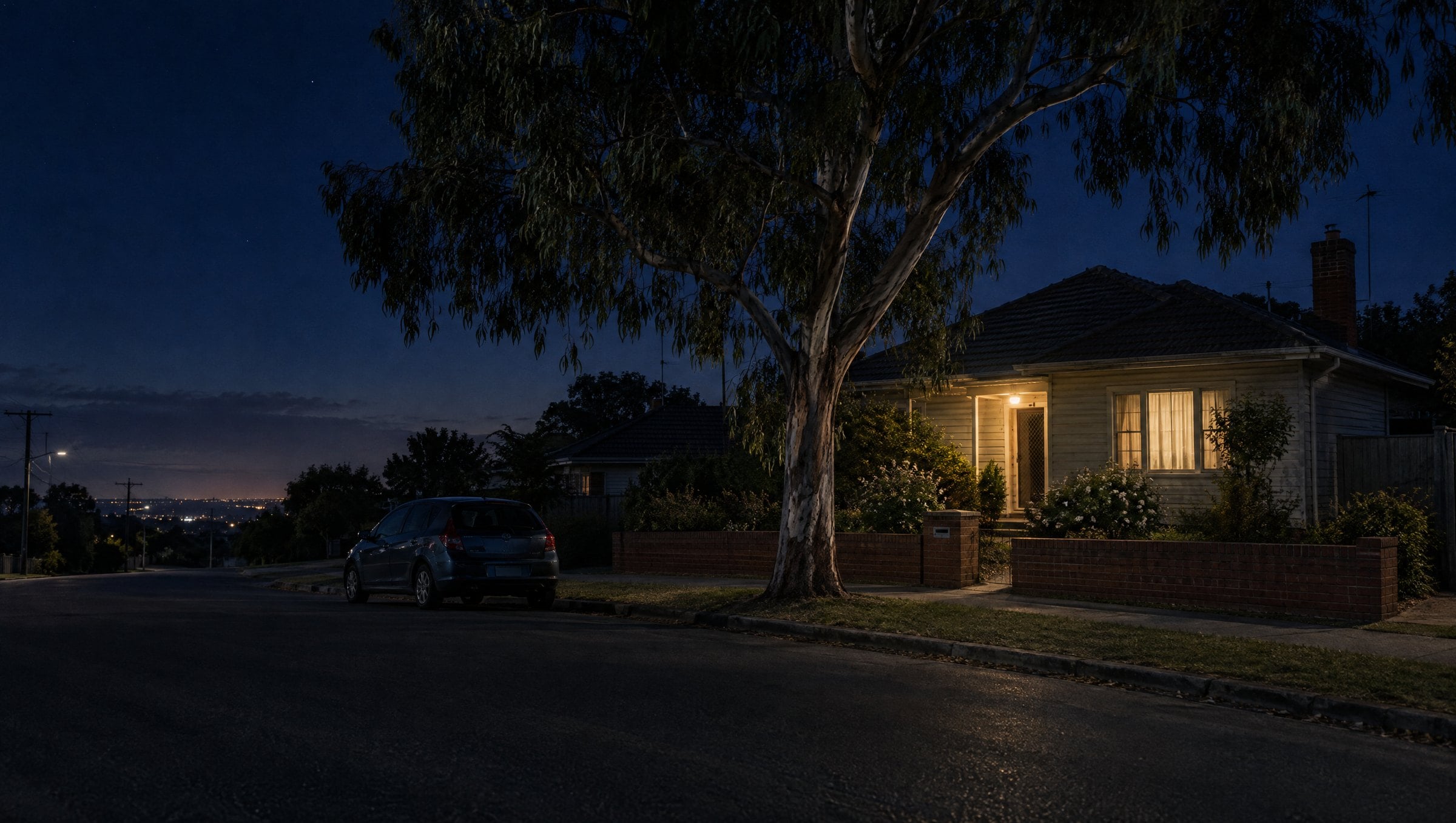 An ordinary suburban house at night with the porch light on, seen from across a quiet street